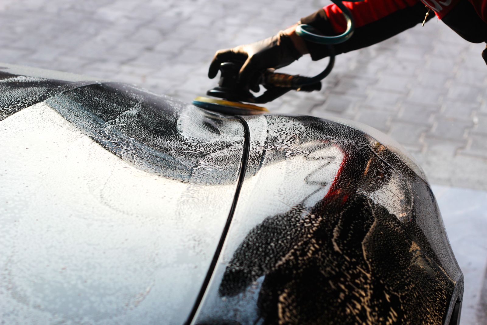 Gloved hands hand-waxing and polishing a car's gleaming paintwork under studio light