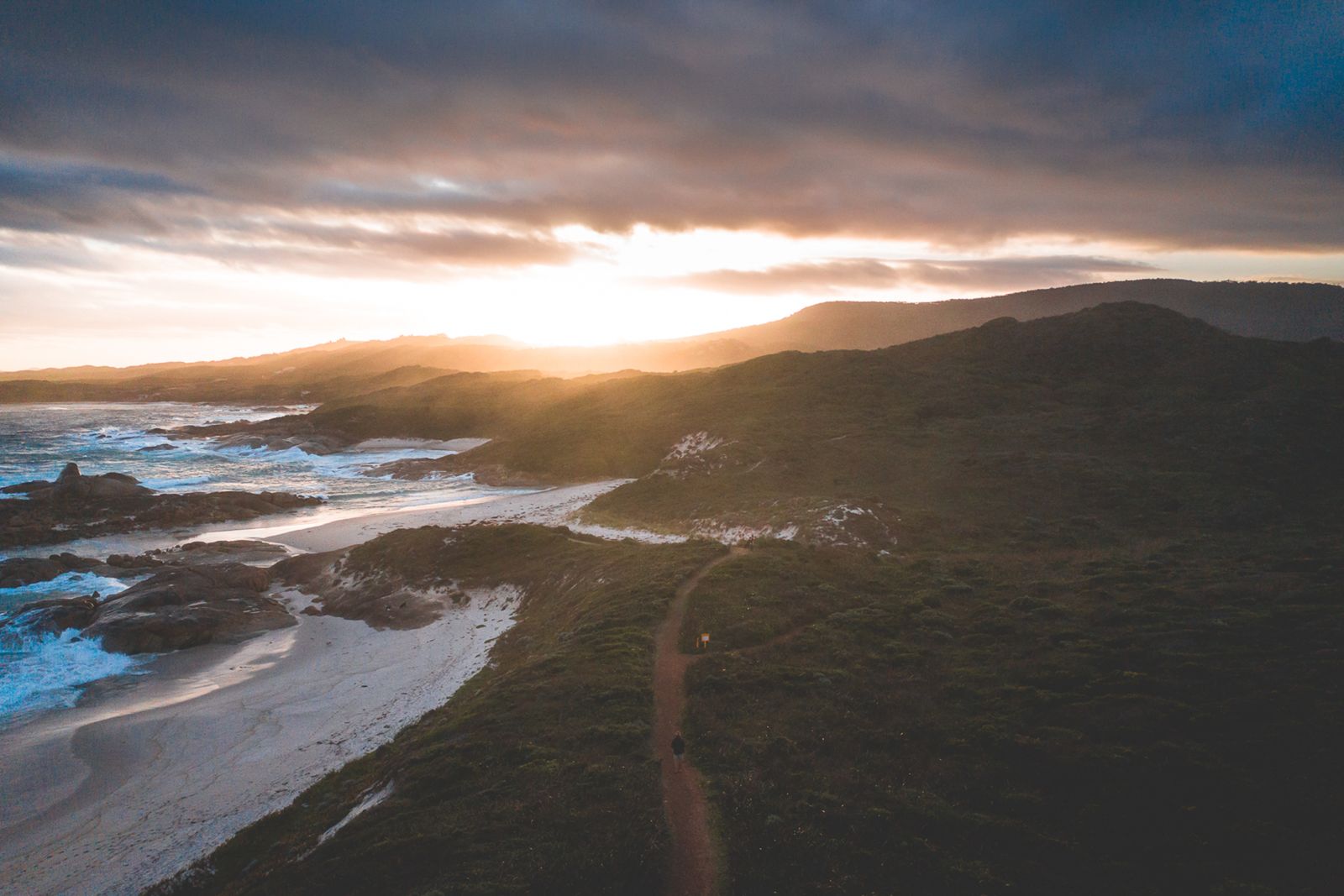 Aerial view of a rugged coastline during sunset with waves crashing on the shore