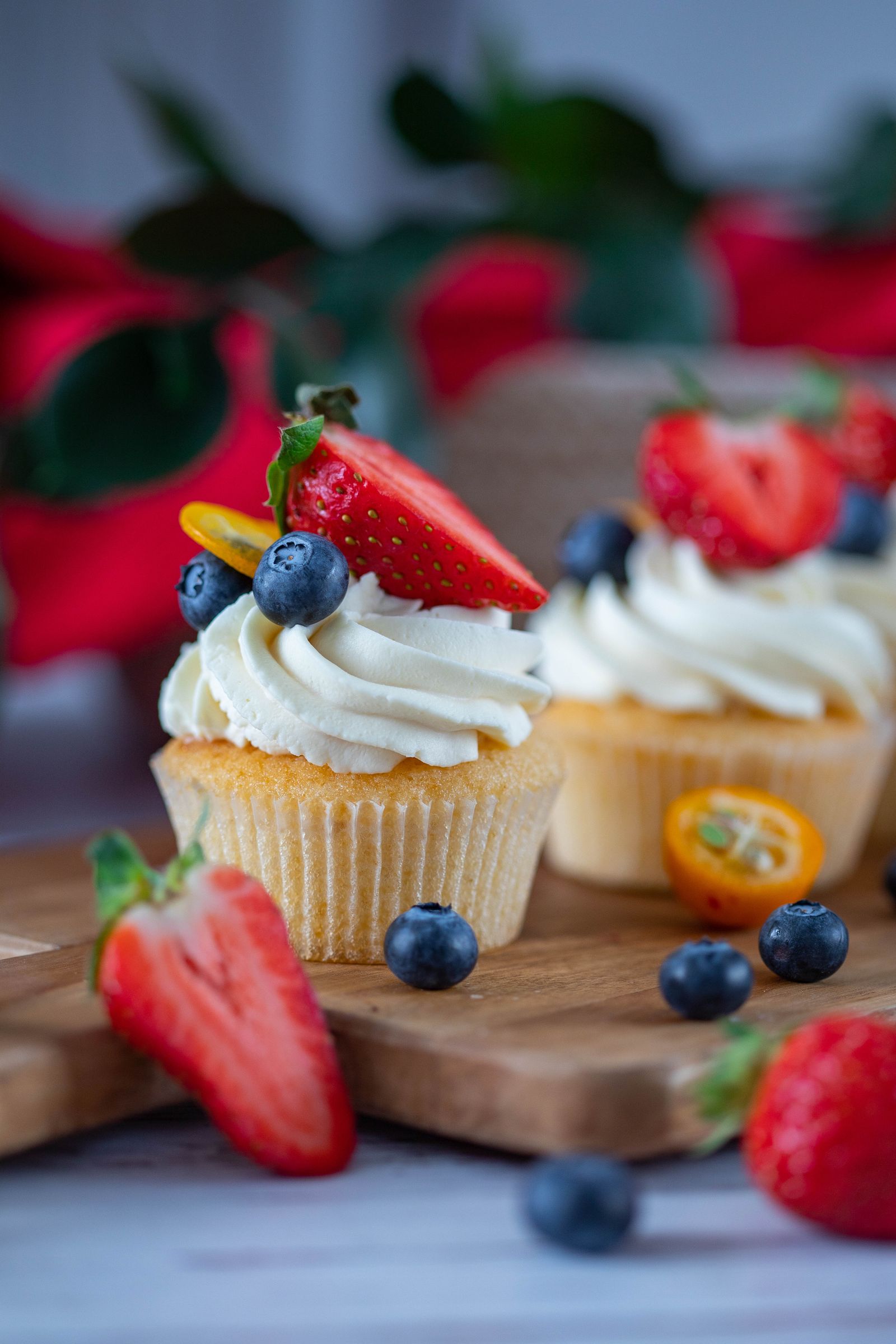 Cupcakes topped with fresh strawberries and blueberries on a wooden board