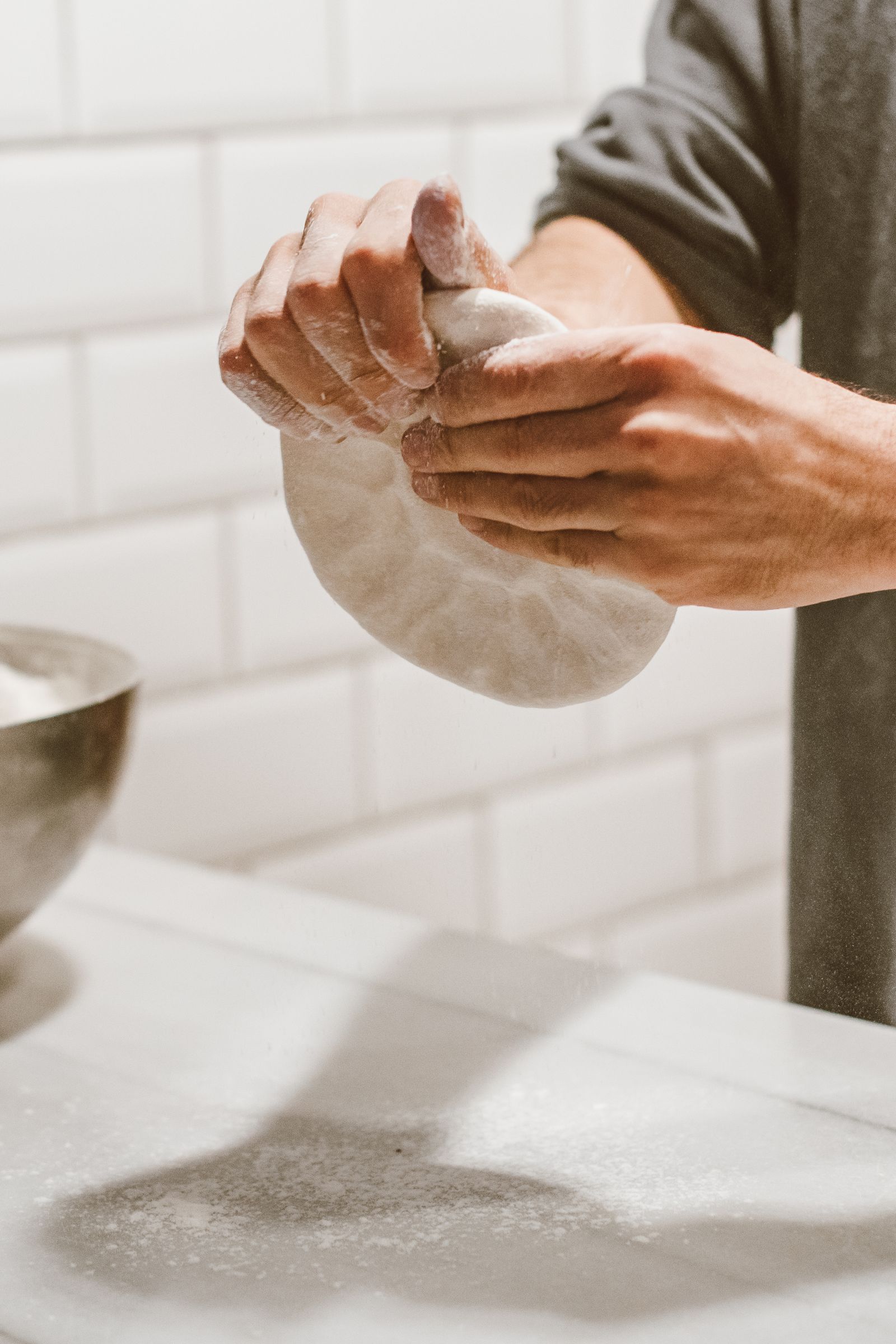 A baker's hands kneading dough on a marble countertop