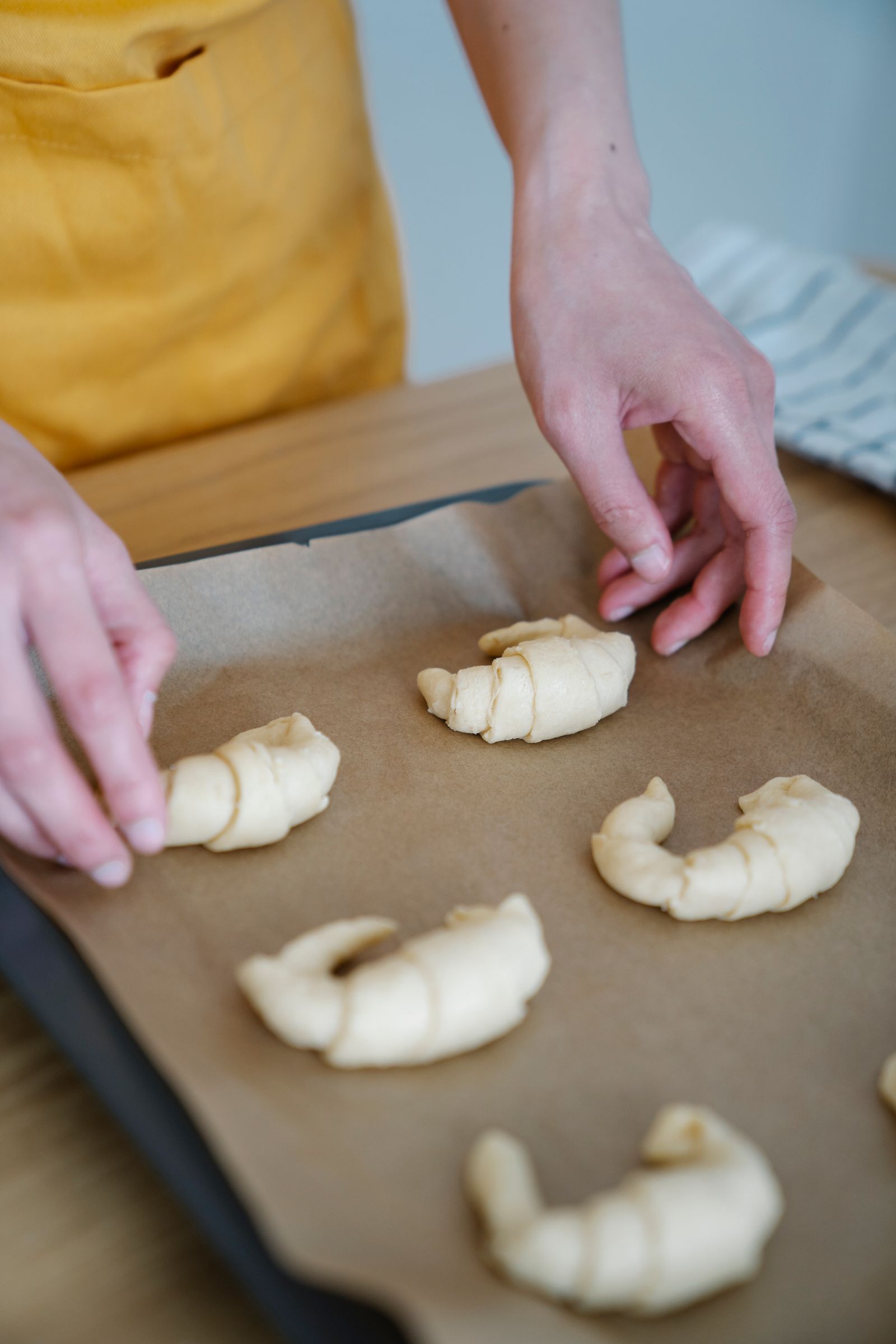 A pastry chef's hands shaping croissants on a paper-lined baking tray