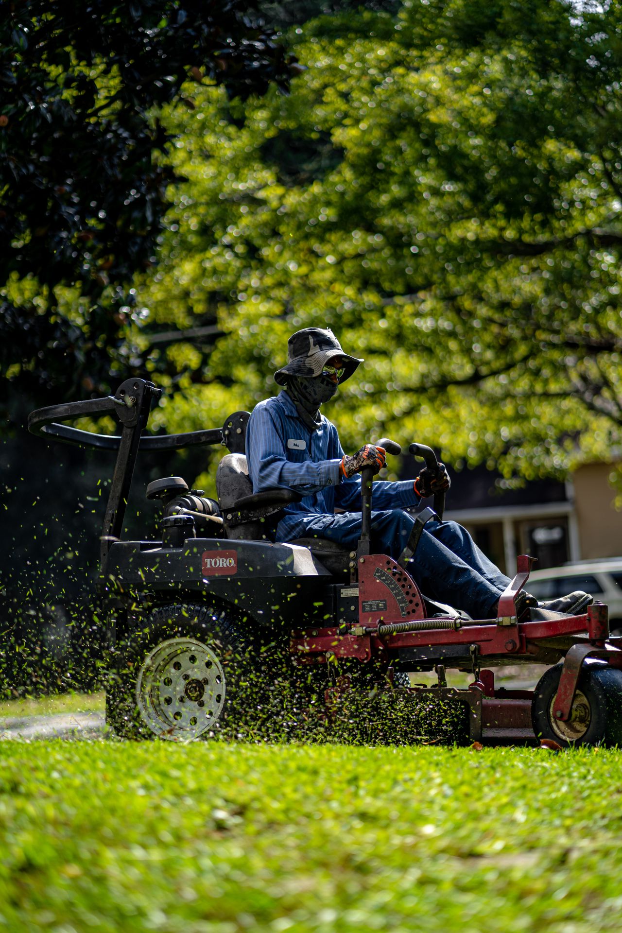 Landscaper riding a zero-turn mower across a lush lawn, grass clippings flying