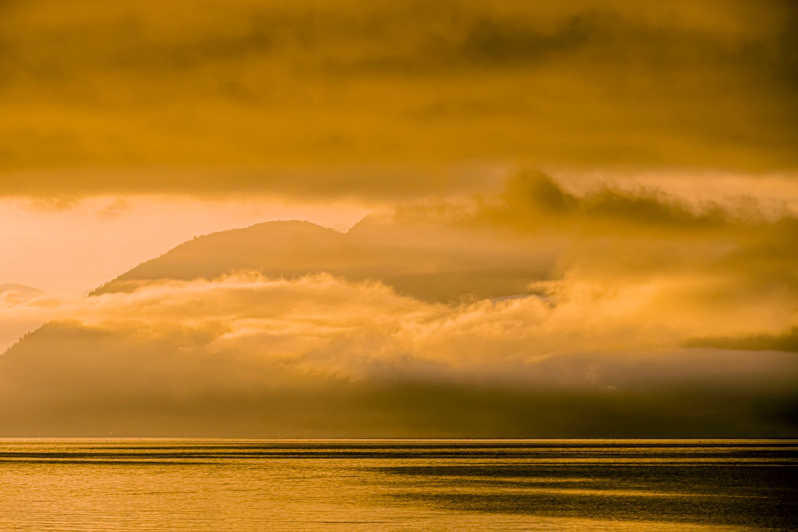 Golden sunrise light over misty mountain peaks with a calm lake below
