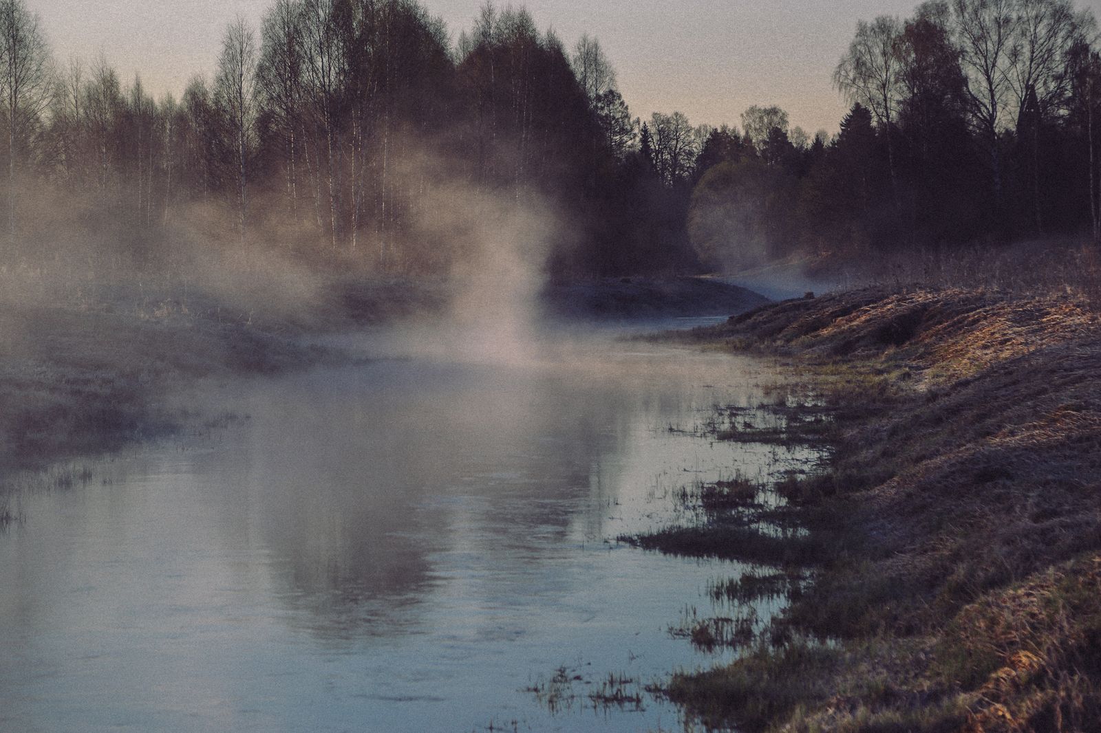 Misty river winding through a wooded landscape lit by soft morning sunlight