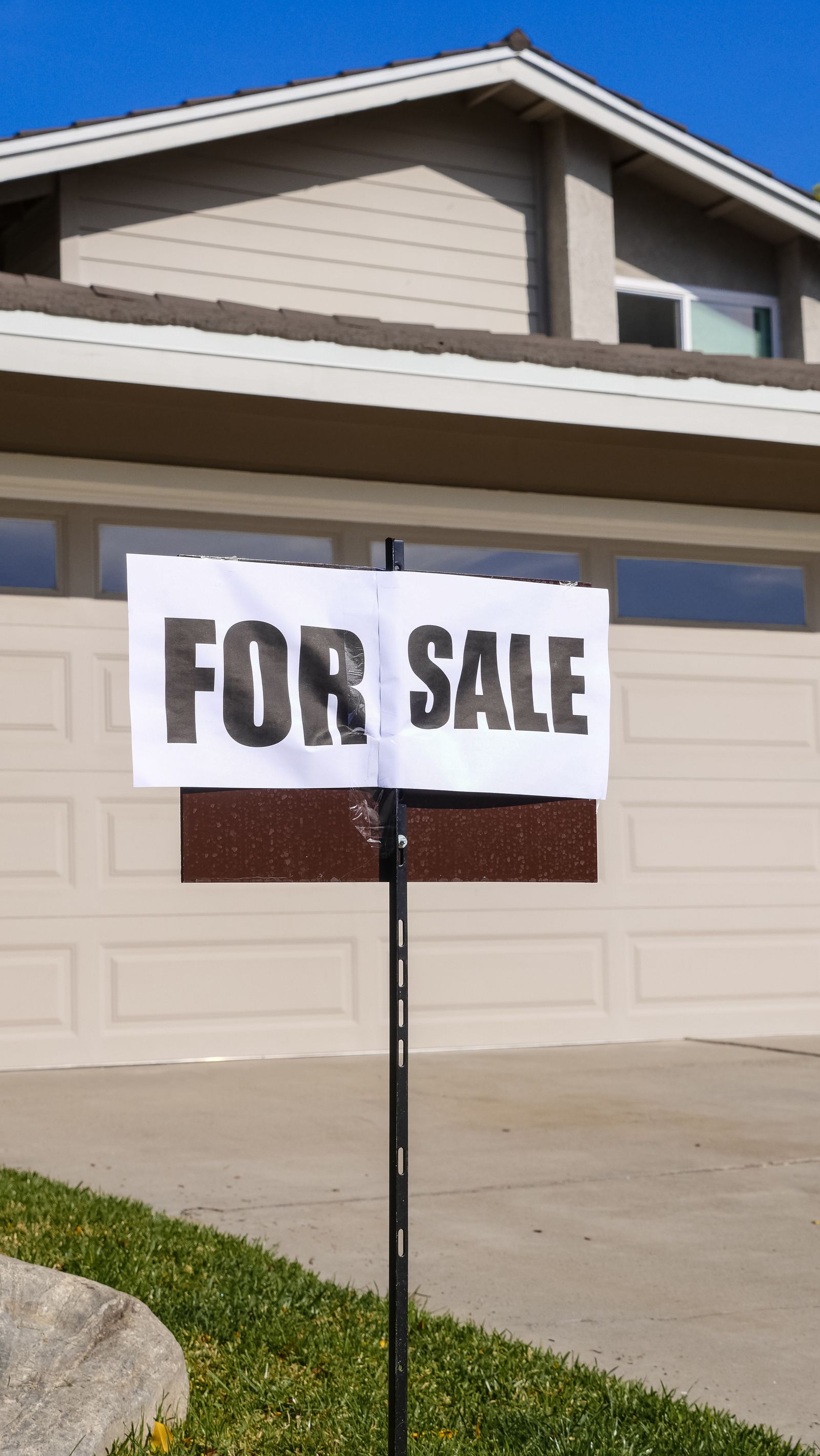 A For Sale sign in the front yard of a suburban house