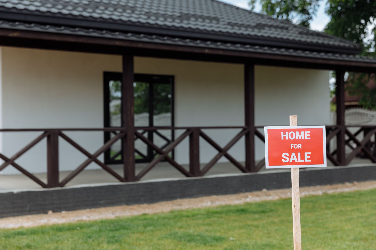 White house with a front porch and a Home for Sale sign on a sunny day