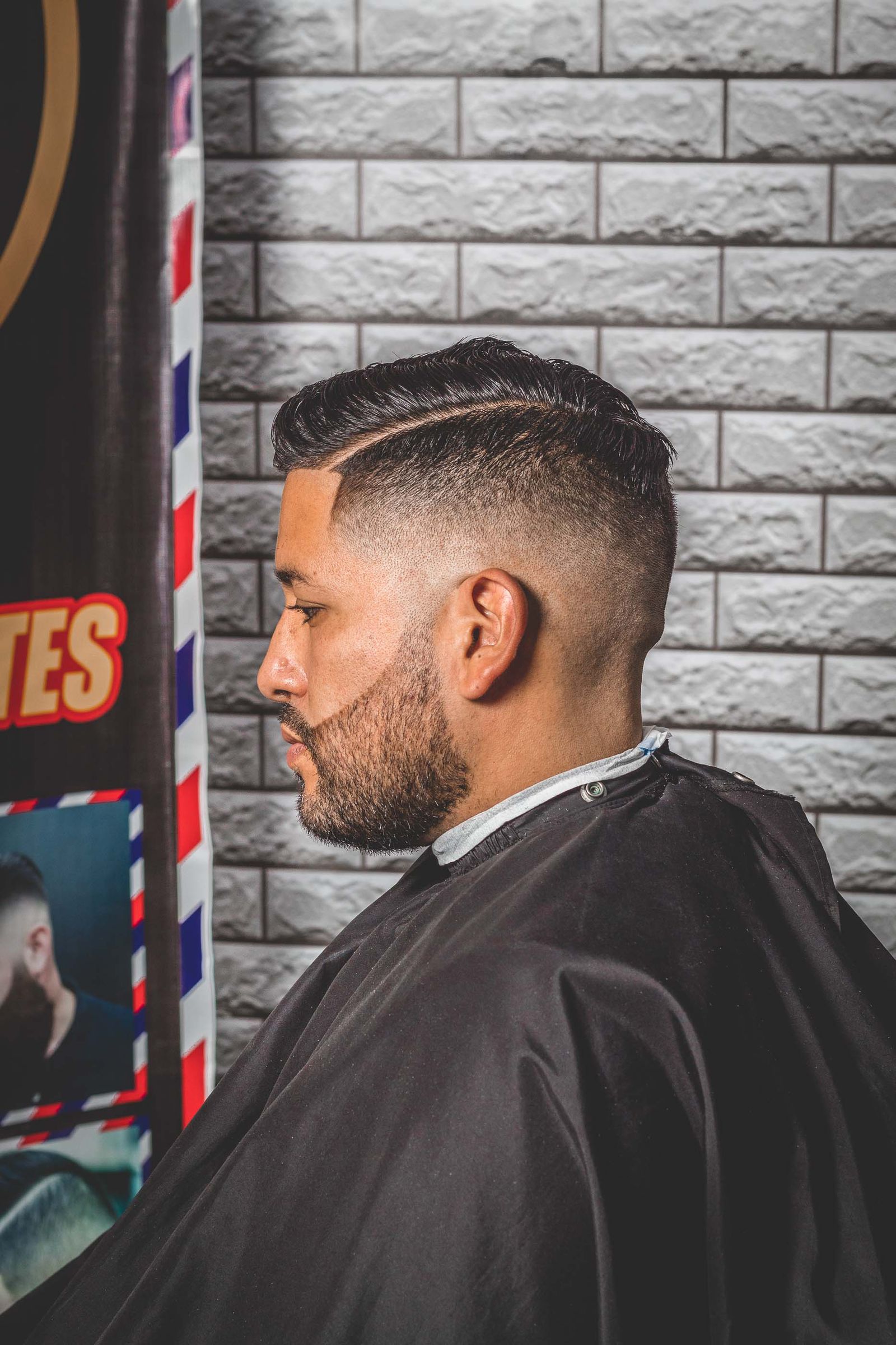 Profile view of a man seated at a barber shop mid-service