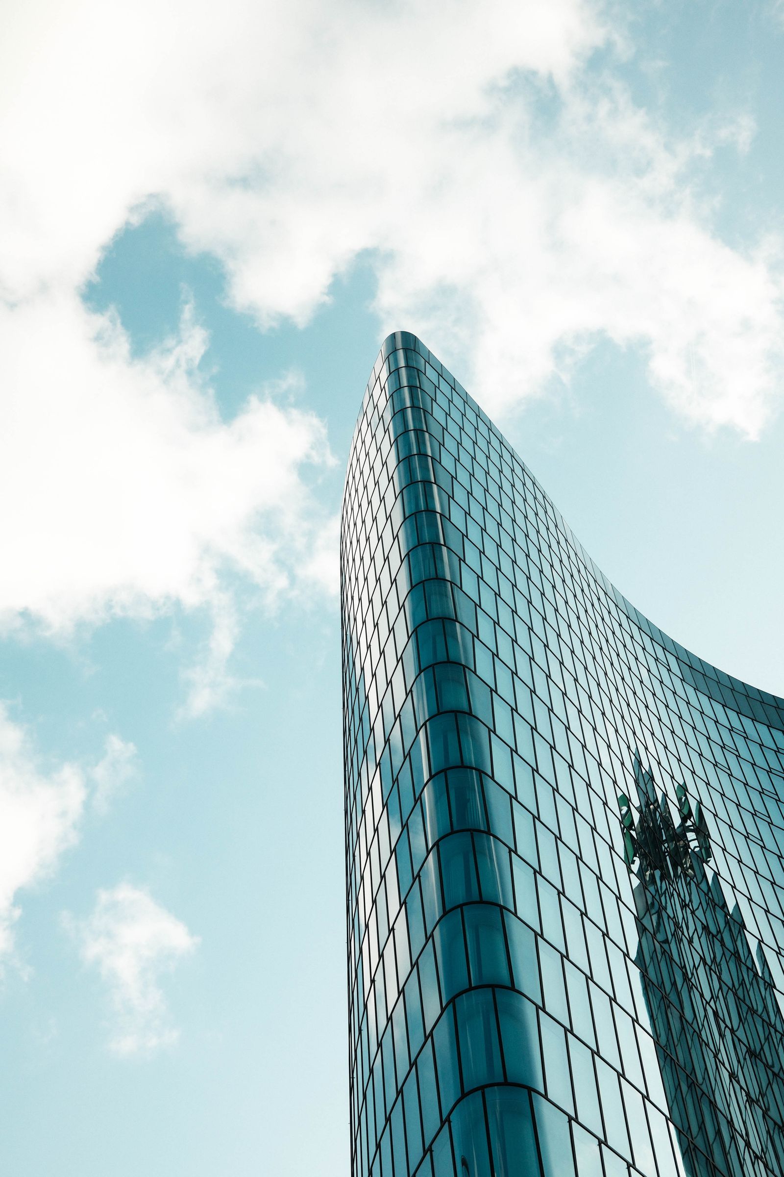 Sleek curved glass skyscraper facade sweeping against a vibrant blue sky with clouds